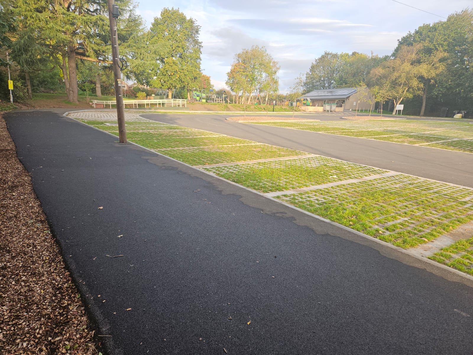 Tarmac footpath and access road beside grass reinforcement parking bays within a public open space.