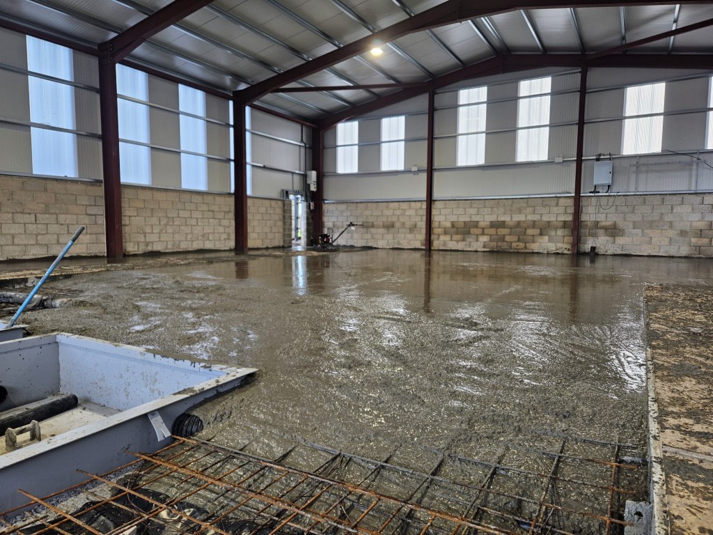 Freshly poured concrete floor slab inside a steel-framed industrial building.